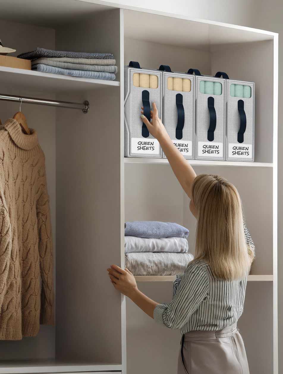 Woman reaching for beige NeatlyThere bed sheet organizers labeled Queen Sheets on a linen closet shelf
